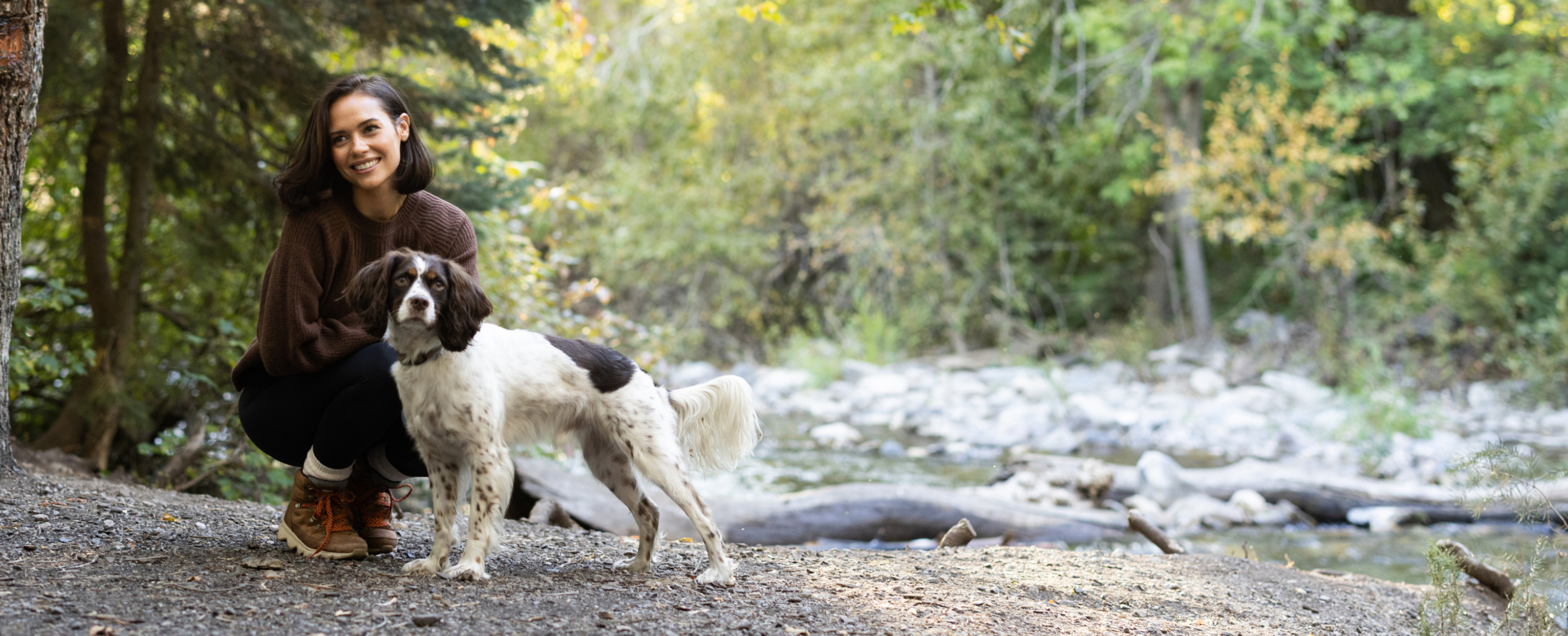 Woman kneeling with dog in woods