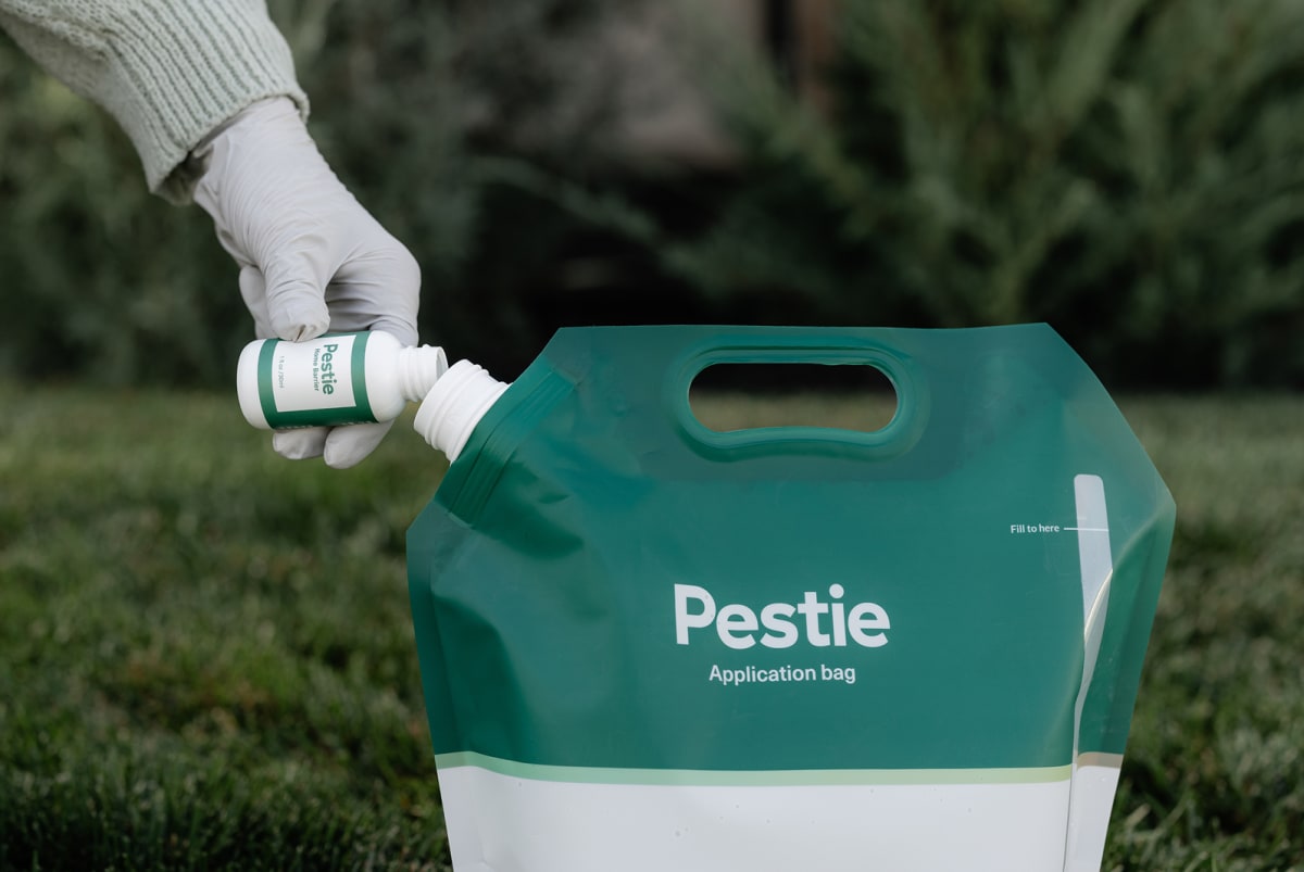 Hand with glove pouring Pestie home barrier pesticide into bag.
