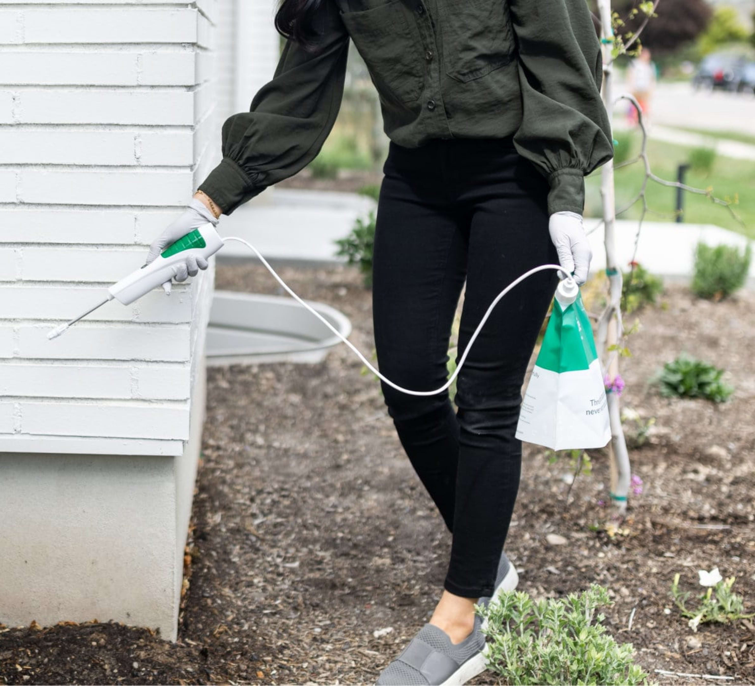 Woman spraying Pestie on the base of a house