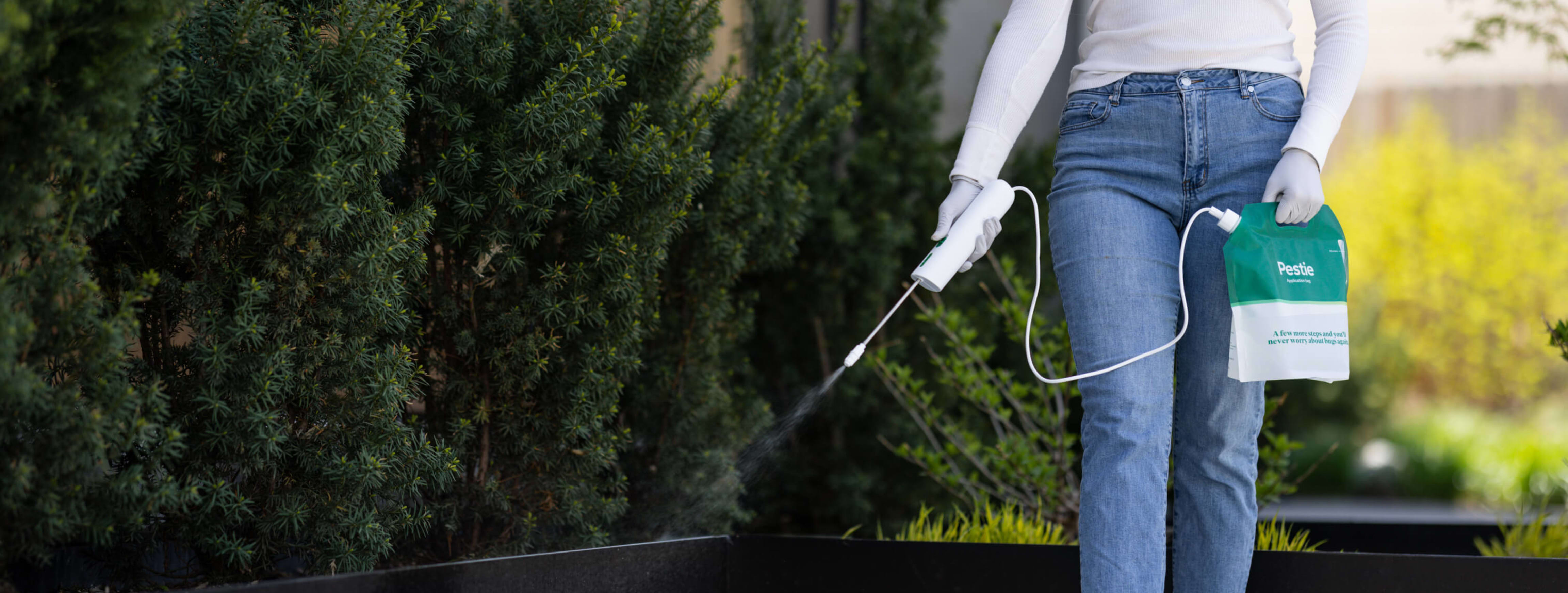 Woman spraying Pestie near planterboxes.
