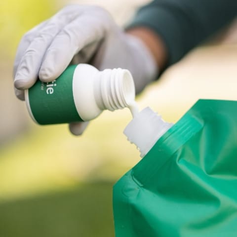 Hand with glove pouring Pestie home barrier pesticide into bag.