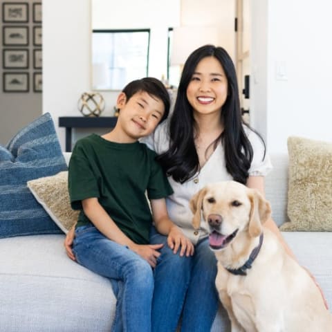 Woman with her child sitting on a couch with a dog infront.