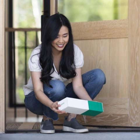 Woman crouched down holding Pestie box at the frontdoor.