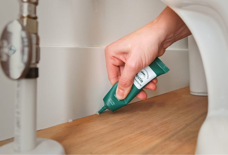 Ant gel bait being placed behind a toilet or vanity.