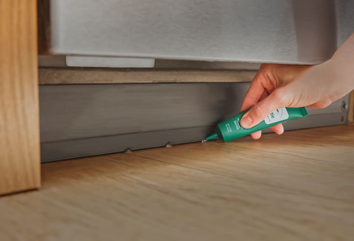 Ant gel bait being placed near a large appliance.